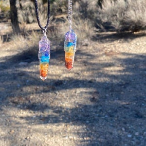 May include: Two chakra necklaces with seven different colored stones, each wrapped in silver wire. The necklaces are on black and silver chains.