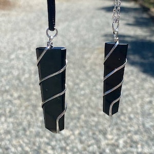 May include: Two black gemstone pendants wrapped in silver wire. The pendants are hanging from black cords and silver chains.