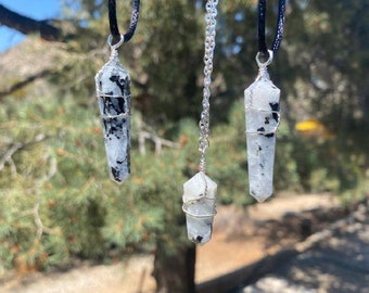 May include: Three silver wire wrapped crystal pendants on different chains. The crystals are white with black flecks and are shaped like long, thin points. The chains are black, silver, and black.