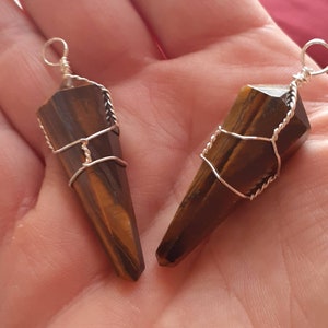May include: Two gold-wrapped tiger's eye crystal pendants. The crystals are pointed and have a brown and gold color.