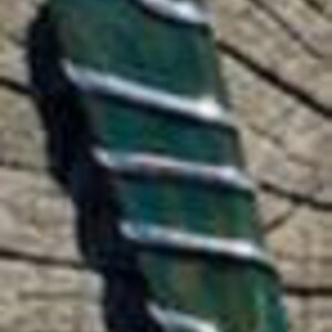 Pu&ograve; includere: Un ciondolo in pietra verde con filo d'argento avvolto attorno. Il ciondolo ha una forma rettangolare allungata e una texture ruvida e naturale.