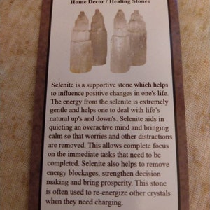 May include: A rectangular informational card with a brown border featuring a graphic of four off-white selenite stone towers. The text reads Selenite Home Decor / Healing Stones followed by a paragraph describing the properties of the stone.