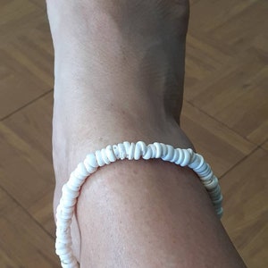 May include: White shell anklet with a simple design. The anklet is made of small, white shells that are strung together on a clear string.