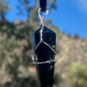 May include: A black obsidian crystal point pendant on a black velvet cord. The crystal is wrapped in silver wire.
