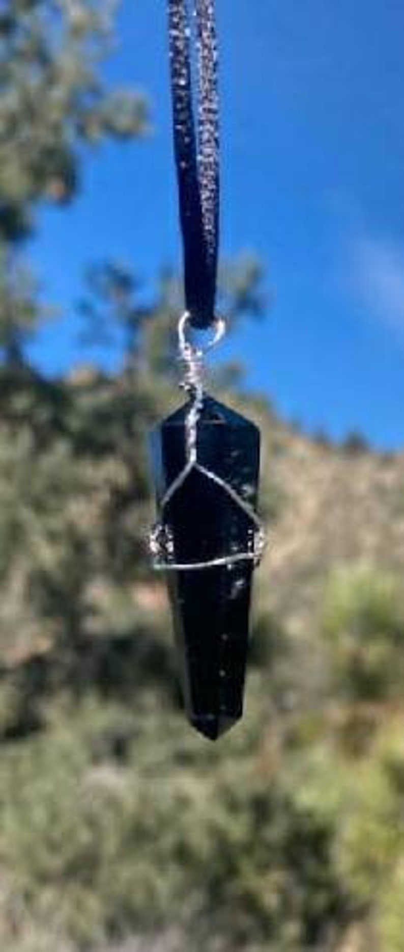May include: A black obsidian crystal point pendant on a black velvet cord. The crystal is wrapped in silver wire.