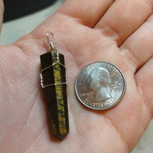May include: A gold and black tiger's eye crystal point pendant wrapped in silver wire. The pendant is about the size of a US quarter.