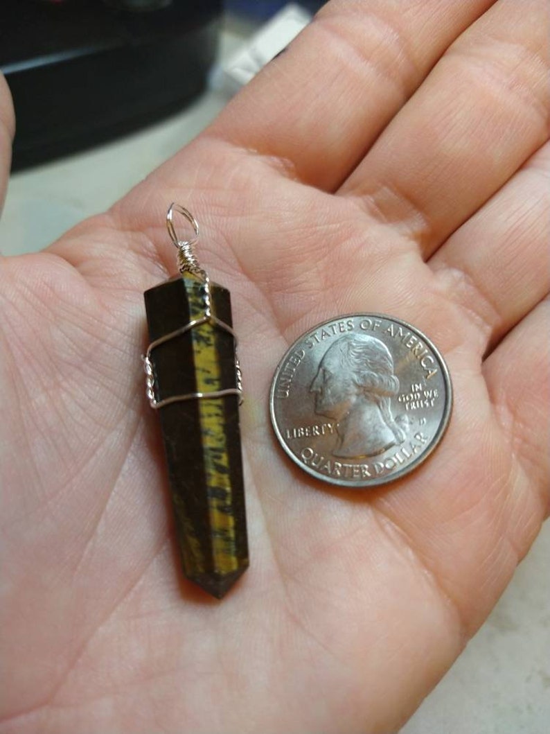 May include: A gold and black tiger's eye crystal point pendant wrapped in silver wire. The pendant is about the size of a US quarter.