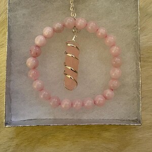 May include: A pink rose quartz bracelet and pendant set in a silver gift box. The bracelet is made of round, light pink beads. The pendant features a rose quartz crystal wrapped in silver wire, suspended from a delicate chain.