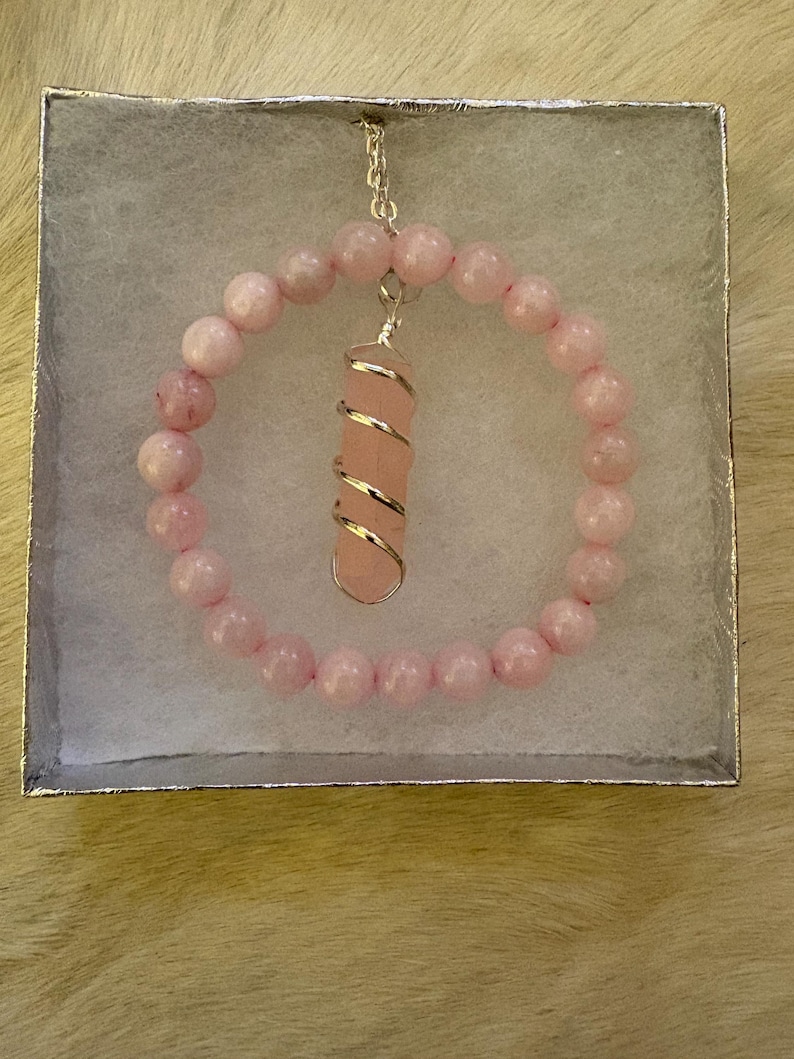 May include: A pink rose quartz bracelet and pendant set in a silver gift box. The bracelet is made of round, light pink beads. The pendant features a rose quartz crystal wrapped in silver wire, suspended from a delicate chain.