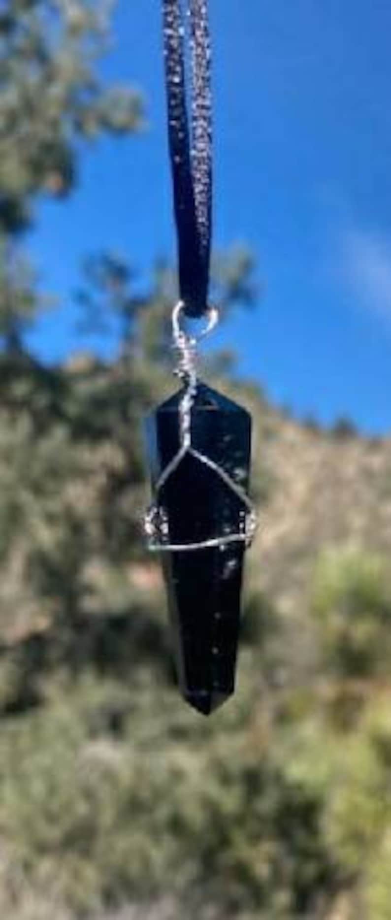 May include: A black obsidian crystal point pendant on a black velvet cord. The crystal is wrapped in silver wire.