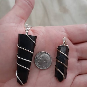 May include: Two black crystal pendants wrapped in silver wire. The larger pendant is about the size of a UK ten pence coin.