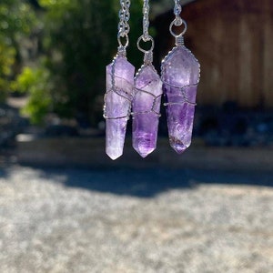 May include: Three amethyst crystal pendants wrapped in silver wire, hanging from silver chains.