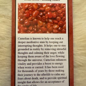 Op de afbeelding: Een kaart met het woord "Carnelian" en de tekst "Home Decor / Healing Stones". De afbeelding toont een close-up van talrijke gepolijste, rood-oranje carnelian stenen. De kaart bevat ook tekst over de eigenschappen van de steen.