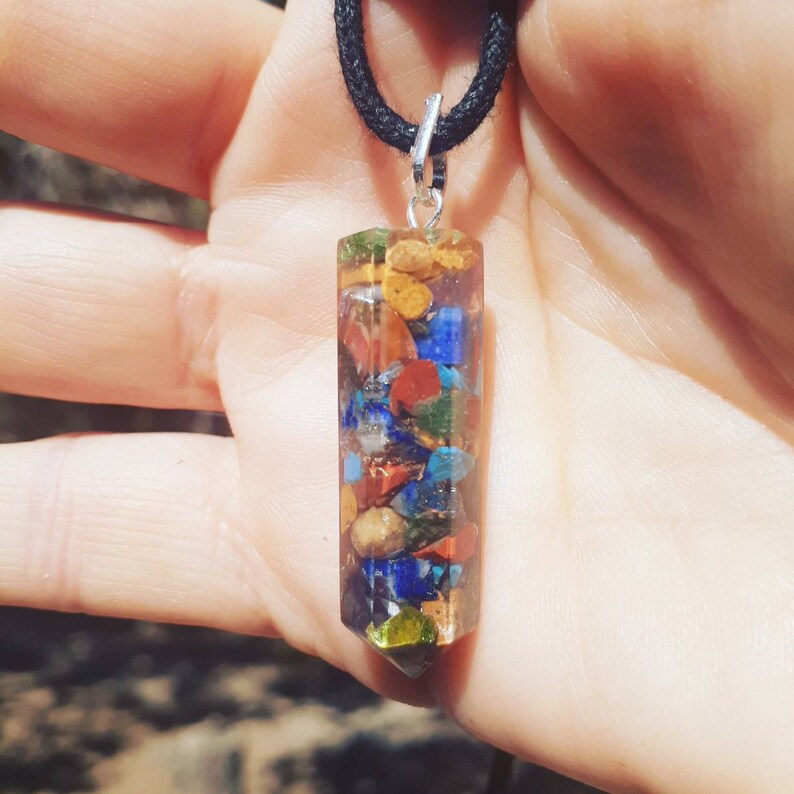 May include: A silver pendant necklace with a clear, faceted, crystal-like charm. The charm is filled with small, colorful stones, including red, orange, yellow, green, blue, and purple.