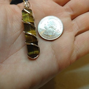 May include: A gold and brown tiger's eye stone pendant wrapped in silver wire. The pendant is about the size of a US quarter.