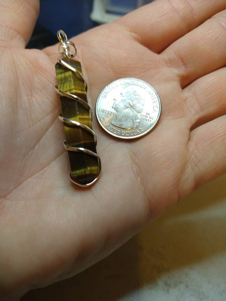 May include: A gold and brown tiger's eye stone pendant wrapped in silver wire. The pendant is about the size of a US quarter.