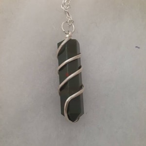 Pu&ograve; includere: Una collana con catena d'argento con un ciondolo di cristallo verde scuro avvolto in filo d'argento.
