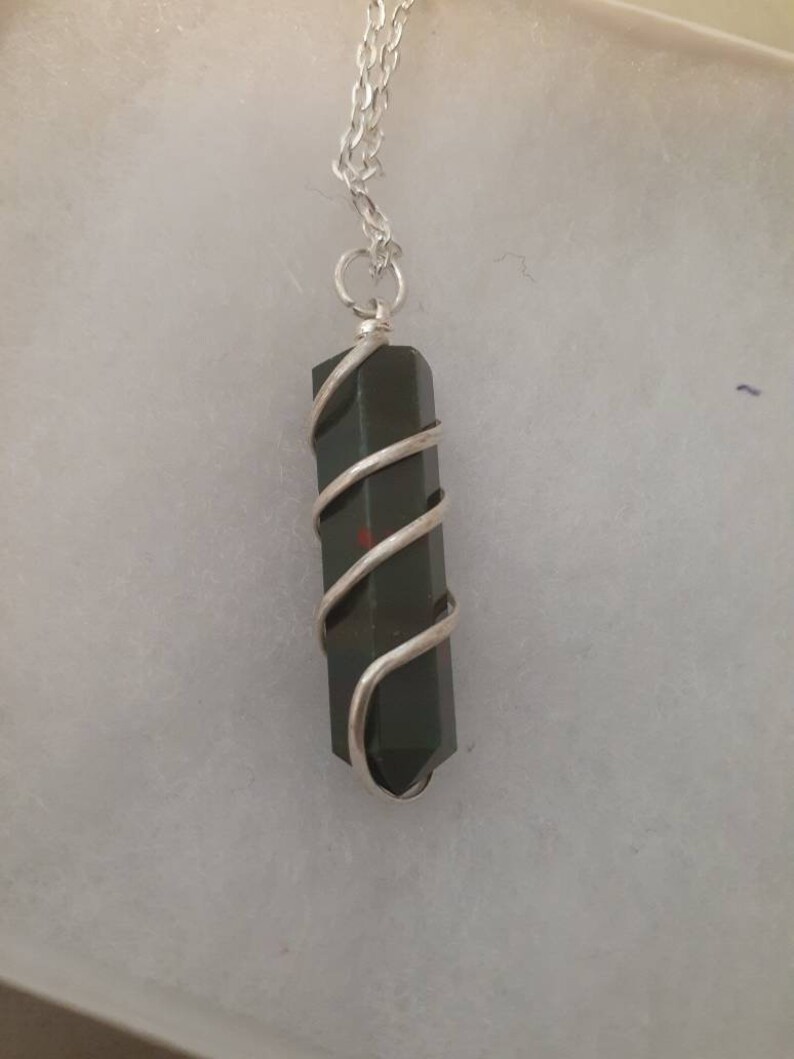 Pu&ograve; includere: Una collana con catena d'argento con un ciondolo di cristallo verde scuro avvolto in filo d'argento.