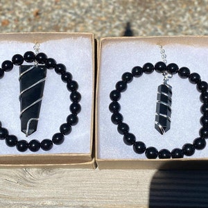 May include: Two black onyx bracelets with silver wire wrapped black onyx pendant charms. The bracelets are in small cardboard boxes with white interiors.