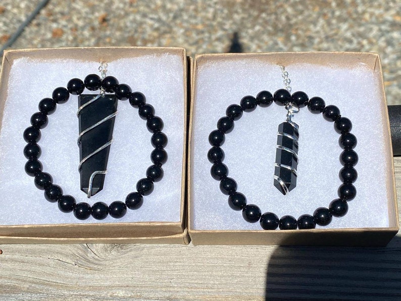 May include: Two black onyx bracelets with silver wire wrapped black onyx pendant charms. The bracelets are in small cardboard boxes with white interiors.