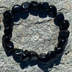 May include: A black gemstone bracelet made with smooth, rounded beads. The bracelet is laid out on a grey, textured surface.