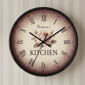 May include: A round wall clock with a black frame. The clock face is cream-colored with Roman numerals and black hands. It features a floral design and the words "Victoria's Kitchen". The clock is mounted on a striped wall.