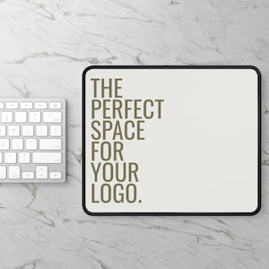 May include: A rectangular mousepad with a black border and the text "THE PERFECT SPACE FOR YOUR LOGO" in brown. A white keyboard is visible on the left side of the image, set against a marble-patterned surface.