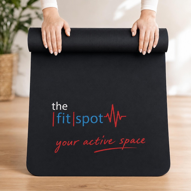 May include: A black rectangular yoga mat featuring the white text 'the', blue text 'fit|spot' with a red heartbeat line graphic, and the red text 'your active space' underlined with a red line. The mat is partially rolled at the top edge.