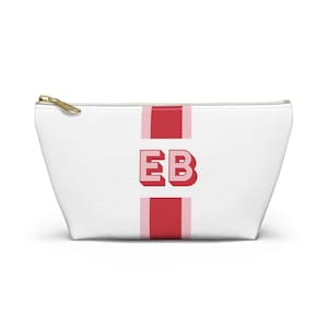 May include: White canvas zippered pouch with a red and pink stripe down the center. The initials "EB" are in bold red letters on the stripe.