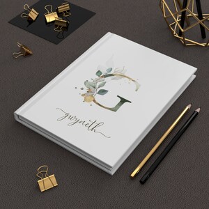 May include: White journal with a watercolor illustration of a green leafy branch and the letter G in gold and green. The name "gwyneth" is written in cursive below the illustration.
