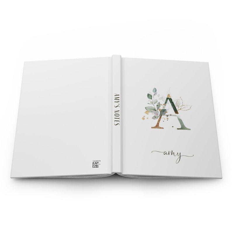 May include: A white notebook with the text "AMY'S NOTES" on the spine. The front cover features a gold and green floral design with the letter "A" and the name "amy" written in cursive.