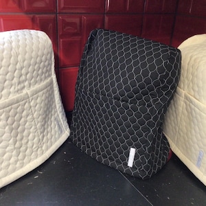 May include: Three quilted appliance covers. Two are cream, and one is black with a white net pattern. The covers have a pocket on the front and are designed to fit over a kitchen appliance.