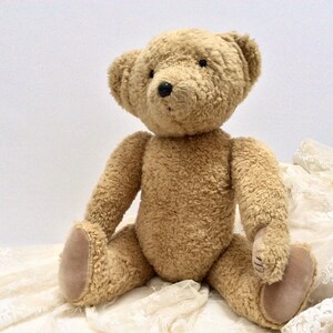 May include: A plush brown teddy bear sitting on a white lace fabric. The bear has a soft, fuzzy texture and black button eyes.