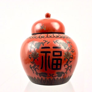 May include: A red ceramic jar with a lid, decorated with black floral patterns and the Chinese character for "fortune" in black.