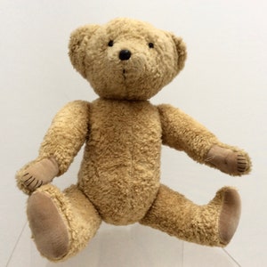 Peut inclure: Un ours en peluche brun clair avec des yeux noirs et un nez brun. L'ours est assis les jambes croisées et les bras tendus.