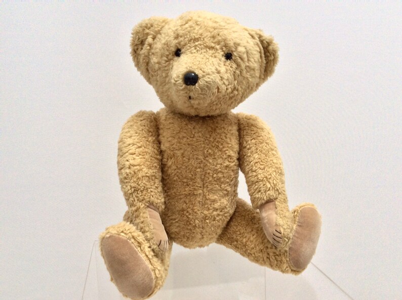 May include: A plush brown teddy bear with black eyes and a black nose. The bear is sitting on a clear surface.