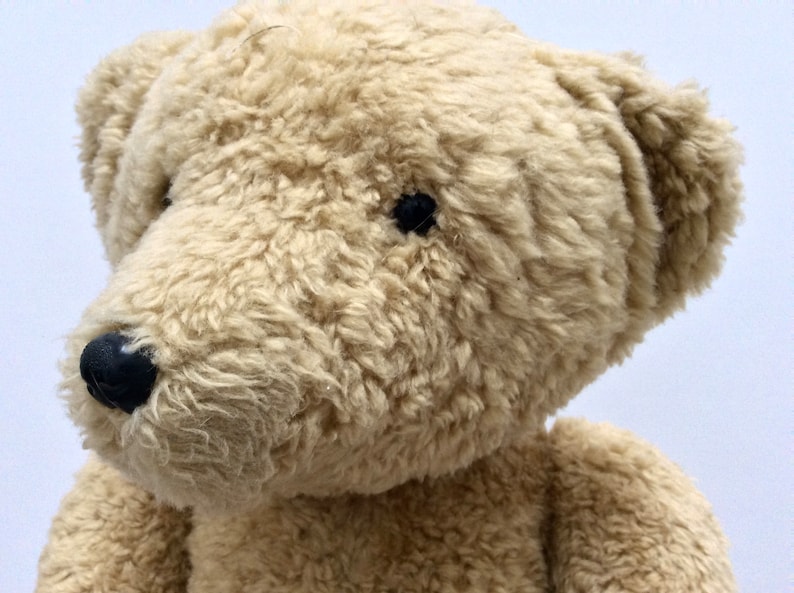May include: A close-up of a beige teddy bear with black eyes and a black nose. The bear's fur is soft and fluffy.