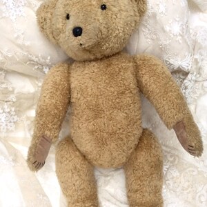 May include: A brown teddy bear with black eyes and a brown nose, lying on a white lace fabric.