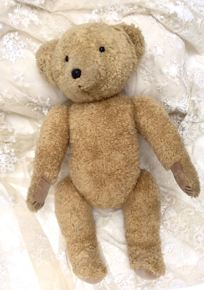 May include: A brown teddy bear with black eyes and a brown nose, lying on a white lace fabric.
