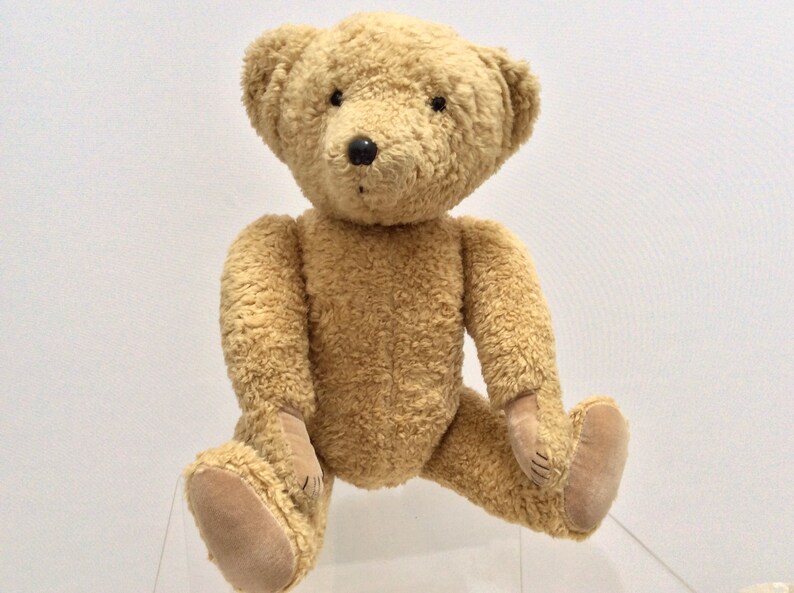 May include: A plush brown teddy bear with black eyes and a black nose. The bear is sitting with its legs crossed and its paws resting on a clear surface.