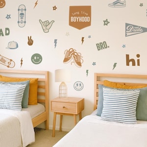 Könnte beinhalten: Ein Schlafzimmer mit zwei Einzelbetten mit hellen Holzrahmen, weißer Bettwäsche und gestreiften Kissen. Die Wand ist mit Skateboard-, Schuh- und Blitzaufklebern sowie den Wörtern "RAD", "BRO" und "hi" dekoriert. Zwischen den Betten befindet sich ein Nachttisch mit einer Lampe.