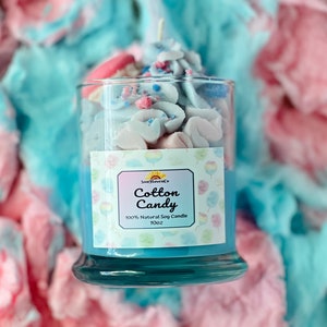 Puede incluir: Un tarro de vela de vidrio azul con una etiqueta blanca que dice "Sun Haven Co. Cotton Candy 100% Natural Soy Candle 10oz". El tarro est&aacute; lleno de una cera de vela blanca y rosa que parece algod&oacute;n de az&uacute;car.