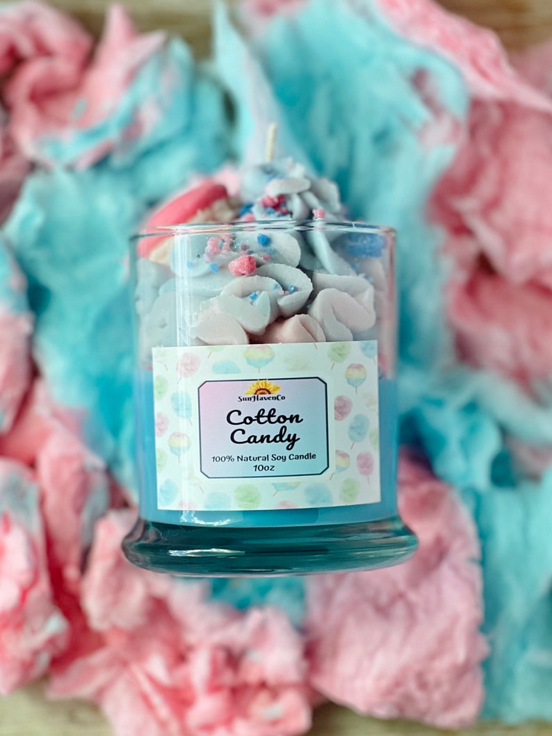 Puede incluir: Un tarro de vela de vidrio azul con una etiqueta blanca que dice "Sun Haven Co. Cotton Candy 100% Natural Soy Candle 10oz". El tarro est&aacute; lleno de una cera de vela blanca y rosa que parece algod&oacute;n de az&uacute;car.