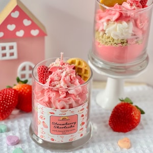 May include: A pink and white strawberry shortcake scented soy candle in a glass jar with a waffle and strawberry on top. The candle is 10oz and 100% natural soy.