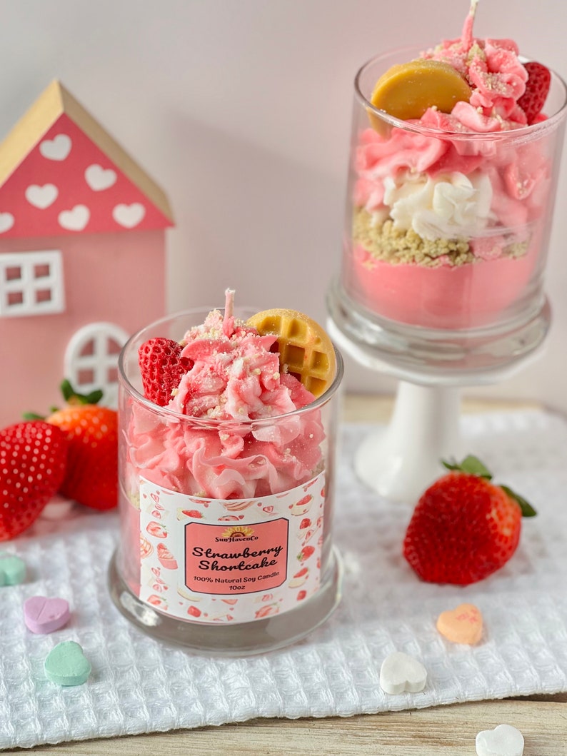 May include: A pink and white strawberry shortcake scented soy candle in a glass jar with a waffle and strawberry on top. The candle is 10oz and 100% natural soy.