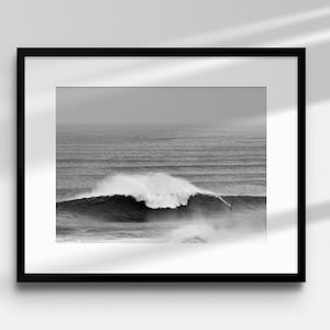 Monochrome ocean wall art featuring a big wave surfer in Nazaré. The image is framed with a white mat and displayed in a neutral-toned room. Perfect for lovers of surfing, minimalism, and Atlantic landscapes. High-quality digital file for large format printing.