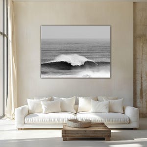 Minimalist living room in soft neutral tones with a large black-and-white ocean wave photograph above a white sofa. Natural light fills the space, highlighting the serene and timeless atmosphere of the Japandi-style interior.