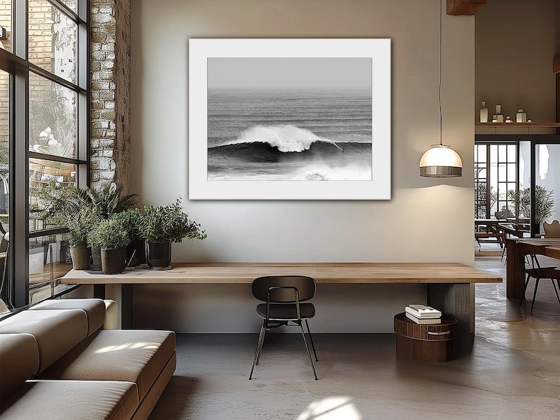 Modern interior with warm wooden textures and potted plants by a large window, featuring a framed black-and-white ocean wave print with a white mat. The soft natural light and earthy materials create a calm, sophisticated ambiance perfect for contemporary wall art.