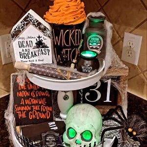 May include: A Halloween display with a black mug reading "Wicked Witch", a "Dead and Breakfast" sign, and a glowing green skull. Other items include a poison bottle, a cauldron, and a rolling pin.