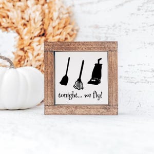 May include: A wooden sign with a white background and black text and images. The sign says "tonight... we fly!" and has images of a broom, a dustpan, and a vacuum cleaner.